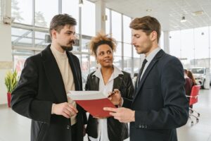 Des professionnels discutent d'un contrat de location ou d'achat de voiture dans une salle d'exposition.