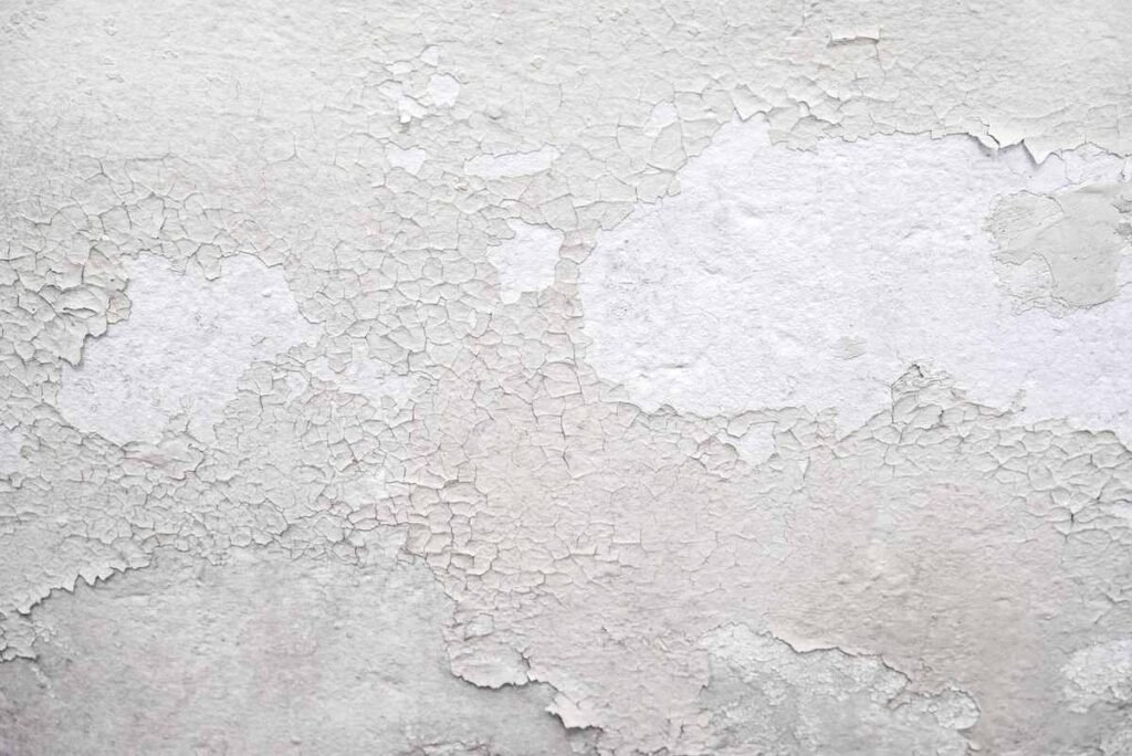 Peinture blanche qui s'écaille sur un mur texturé, montrant sous-couche