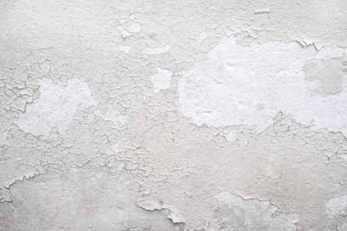 Peinture blanche qui s'écaille sur un mur texturé, montrant sous-couche