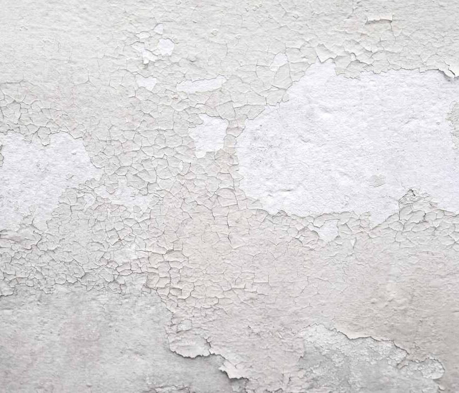 Peinture blanche qui s'écaille sur un mur texturé, montrant sous-couche