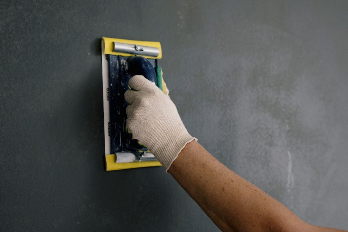 main gantée applique de la pâte noire sur un mur gris