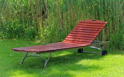Chaise longue en bois rouge posée sur gazon, herbes hautes derrière